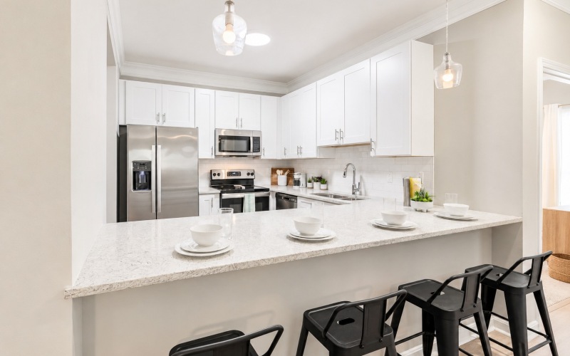 A kitchen with white cabinets, a kitchen island countertop and barstool chairs, and stainless steel appliances at Parker Point apartment complexes in Charleston, SC.