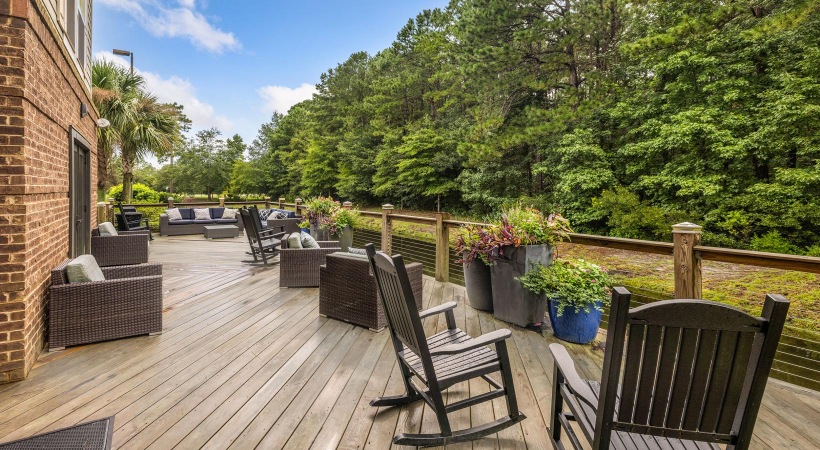 a deck with chairs and tables on it with trees in the back